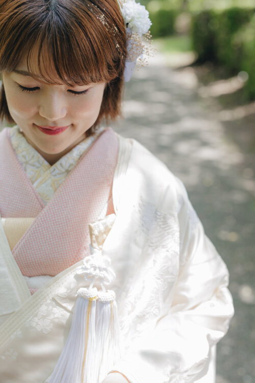 白い花の髪飾りとピンクの衿元、房飾りをアップで写した白無垢の花嫁。和装前撮りで残したい小物と表情