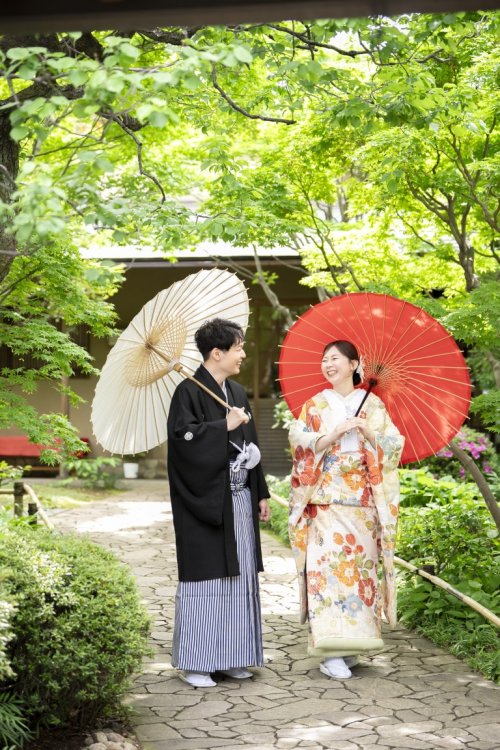 目白庭園で色打掛と紋付姿のおふたりが和傘を手に笑顔で見つめ合う和装前撮り