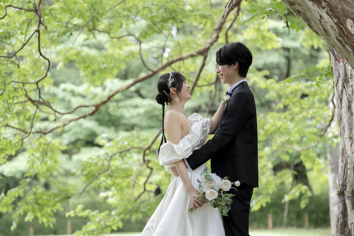木漏れ日の砧公園で見つめ合い笑顔を交わす新郎新婦