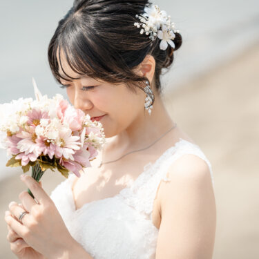 葛西臨海公園にて、花の髪飾りを付けた花嫁が、指輪をはめた手でピンクのブーケに顔を寄せる横顔のアップ。やわらかな光のウェディングフォト