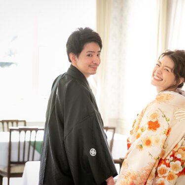 洋館のレストランで振り返って笑う黒紋付の新郎と、橙色の花柄の色打掛の花嫁。明るい光に包まれた和装前撮り