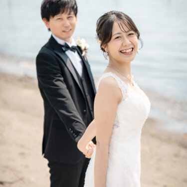 葛西臨海公園にて、赤いバラのブーケを手にした花嫁と新郎が、海辺で振り返ってほほえむ瞬間を切り取った自然体の結婚写真