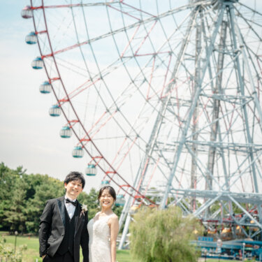 見上げるほど大きな観覧車を背景に、ブーケを持って並ぶタキシードの新郎とマーメイドドレスの花嫁。葛西臨海公園のフォトウェディング