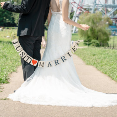 葛西臨海公園の大観覧車を背に、JUST MARRIEDのガーランドを腰に巻いて歩く新郎新婦の後ろ姿。マーメイドラインのドレスの裾が映える前撮り