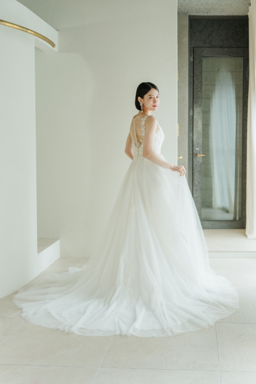 白い部屋で振り返る、背中にボタンの並ぶウェディングドレスの花嫁の後ろ姿。バックスタイルを見せる前撮りのドレスの衣装写真