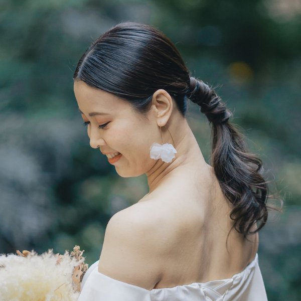 白い花のイヤリングを合わせた低めのポニーテール。オフショルダーのウェディングドレスで微笑む花嫁の前撮りヘア