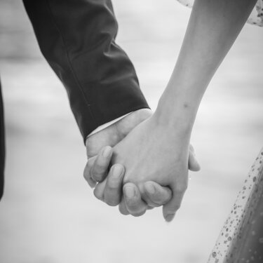 砂浜で手をつなぐ新郎新婦の手元をモノクロで切り取ったカット。チュールのドレスの質感が映える結婚写真