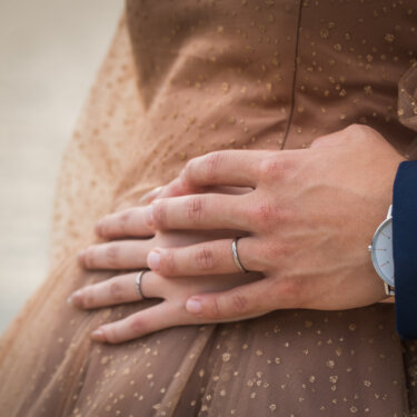 結婚指輪をはめた手を花嫁の腰に重ねる新郎の手元のアップ。きらめくチュールのカラードレスが映える前撮り写真