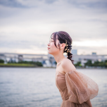 水辺で目を閉じて唇をとがらせる、編み込みのヘアアレンジのカラードレスの花嫁。お台場で撮るかわいい結婚写真