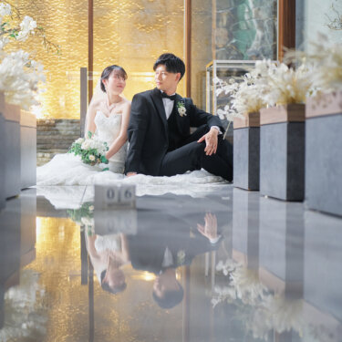 バージンロードに座ってくつろぐ新郎新婦と、手前に置いた日付ブロック。床のリフレクションが美しいチャペルの前撮り