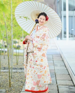 白地に紅葉や毬が映えるレトロな色打掛「琴音小花」に和傘を差し、石畳に立つ花嫁の和装前撮り（衣装番号NMOS03）
