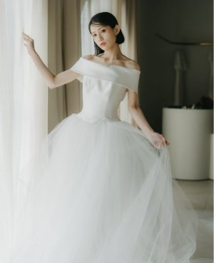 ハツコエンドウのサテンの胸元とチュールを重ねたプリンセスラインのウェディングドレスで、カーテンに手を添える花嫁の前撮り（衣装番号DR03）