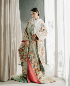 淡いグリーンの地に花車を描いた色打掛に赤い裏地を合わせて窓辺に立つ、表参道店の和装前撮りの花嫁（衣装番号DR03）