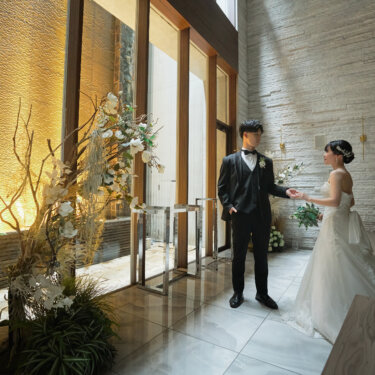 金色に輝く水の壁の前で、花嫁の手を取って向き合う新郎。光と影が美しいチャペルで撮るクラシカルな結婚写真