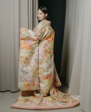 金色とピンクの地に四季の花を描いた色打掛の裾を広げて立つ、表参道店の和装前撮りの花嫁（衣装番号DMOS20）