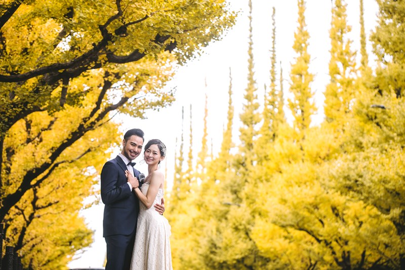 黄色く色づいた外苑いちょう並木の木の下で寄り添う、ウェディングドレスの花嫁とタキシードの新郎