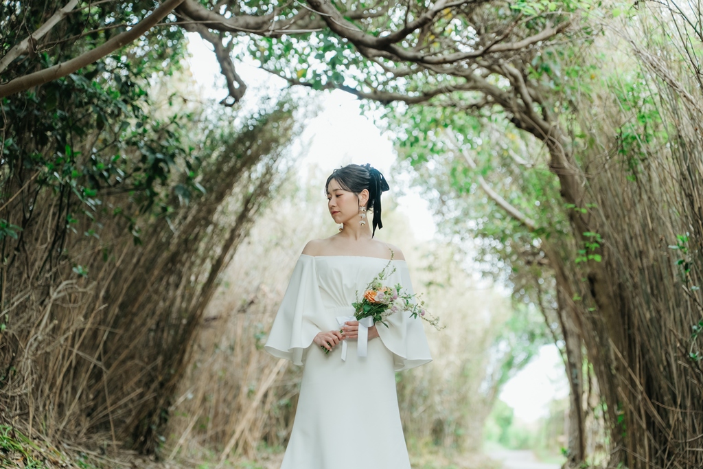 城ヶ島の木々のトンネルの中でブーケを持って立つ、袖のあるウェディングドレスの花嫁