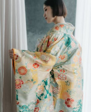 ミントと黄色の地に赤や緑の花が舞う華やかな色打掛の袖を広げ、横を向く花嫁の和装前撮り（衣装番号DMOS19）