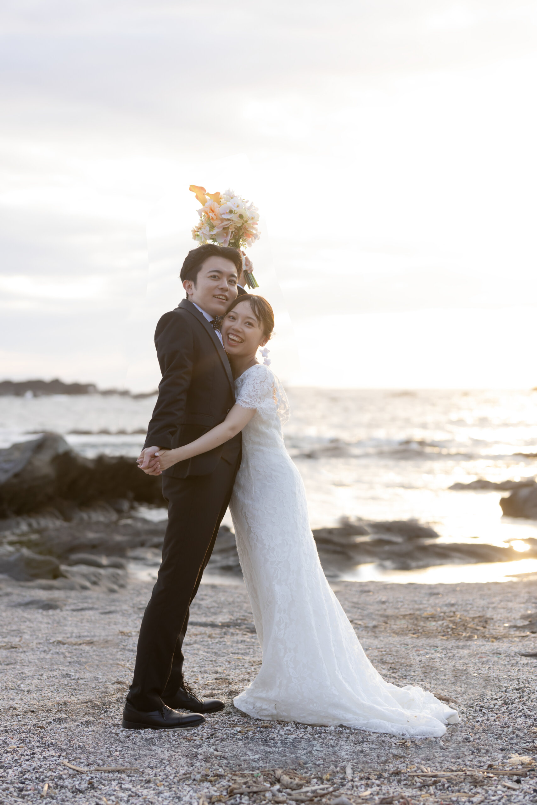 城ヶ島の海辺の岩場に立つ、すっきりとしたシルエットのウェディングドレスの花嫁の全身写真
