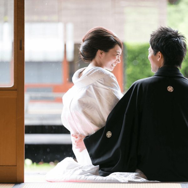 縁側に並んで座る黒紋付の新郎と白い着物の花嫁の後ろ姿。すっきりしたまとめ髪で撮る和装前撮り