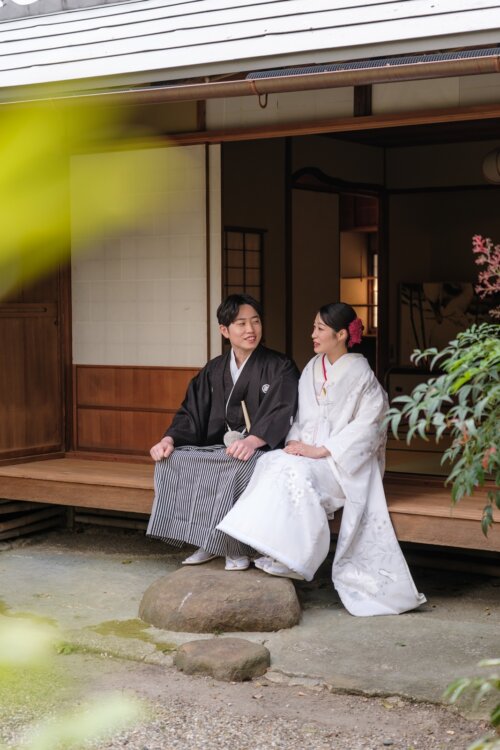 日本庭園の茶室の縁側に並んで座る、黒紋付袴の新郎と白無垢の花嫁。落ち着いた雰囲気の和装の結婚写真
