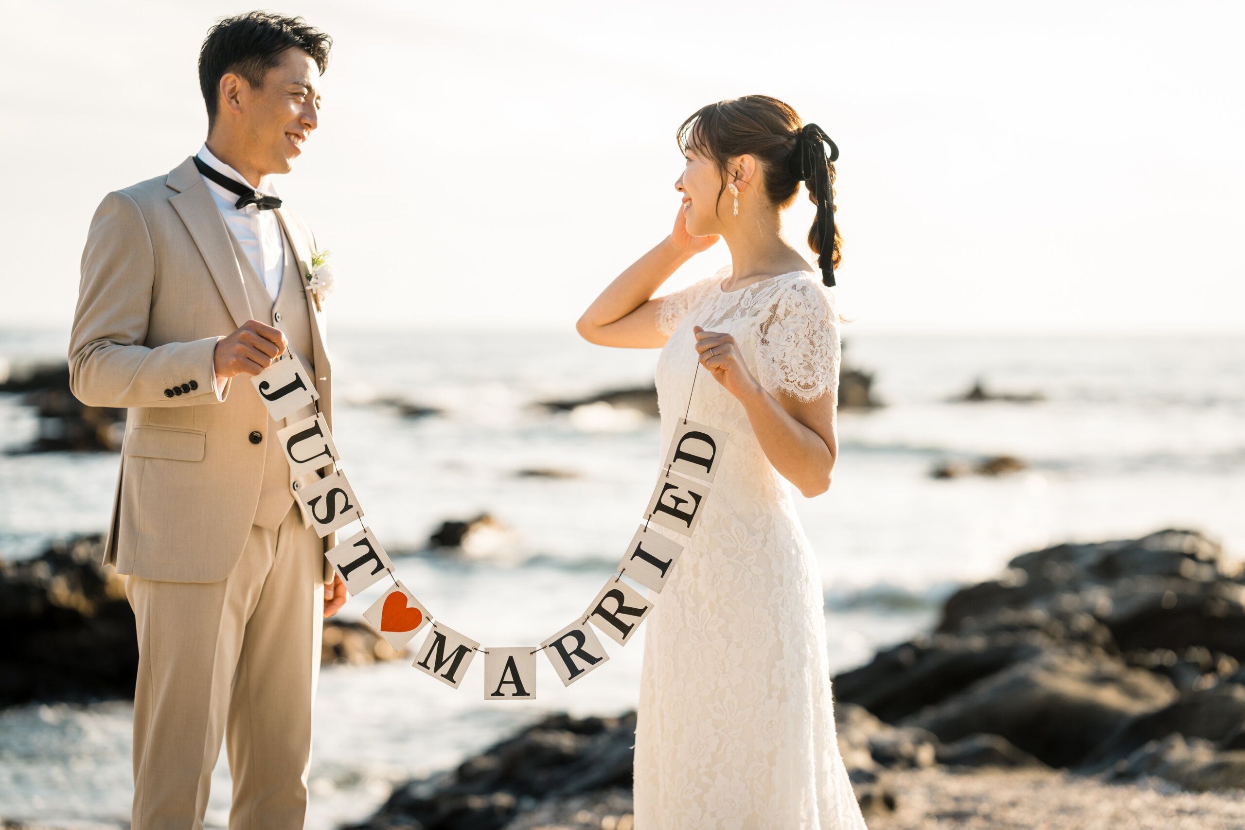城ヶ島の芝生で寄り添う、ブラウンのスリーピースのタキシードの新郎とウェディングドレスの花嫁