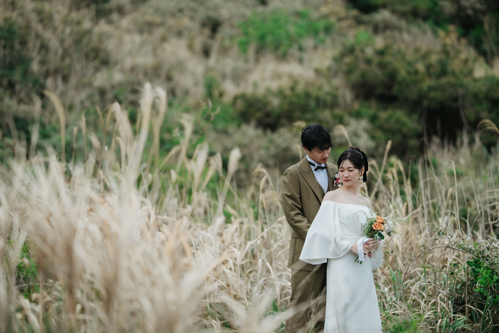 秋の城ヶ島でススキに囲まれて立つウェディングドレスの花嫁と新郎