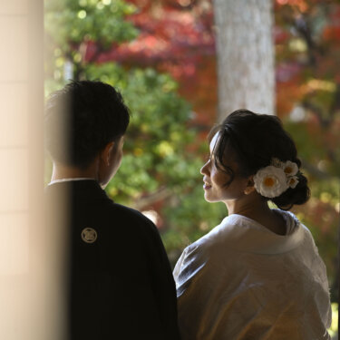 紅葉の庭を望む縁側の陰で、並んで外を見つめる紋付袴の新郎と白無垢の花嫁。日本庭園の紅葉で撮る和装前撮り