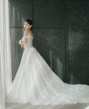 プロノビアスのオフショルダーのウェディングドレスで長いトレーンを広げて立つ花嫁、フォトウェディングで選べるスレンダーラインの一着（衣装番号DC02）