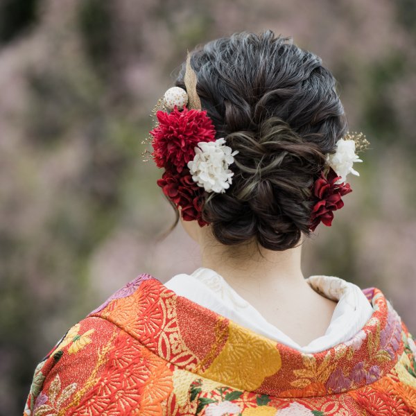 赤い色打掛に合わせた、赤と白の大ぶりな花の髪飾りのふんわりシニヨン。華やかな和装前撮りのヘアスタイル