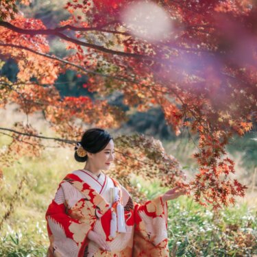 真っ赤なもみじの枝に手を差し伸べて微笑む、鶴柄の赤い色打掛の花嫁。紅葉の和装前撮りで人気の花嫁ソロショット